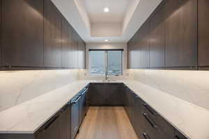 Kitchen featuring light stone counters, modern cabinets, dark wood finish cabinets, a tray ceiling, and recessed lighting