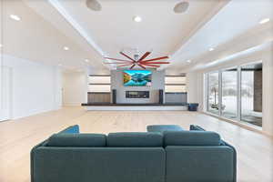 Living area with light wood-style floors, a ceiling fan, a warm lit fireplace, and recessed lighting