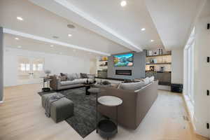 Living area with beam ceiling, light wood-type flooring, a warm lit fireplace, recessed lighting, and french doors