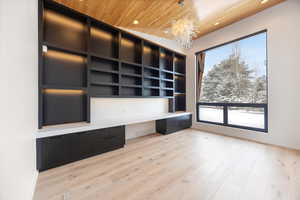 Unfurnished office featuring built in desk, light wood-style floors, hanging lights, and wooden ceiling