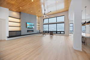 Unfurnished living room featuring a high wood ceiling, a large fireplace, a ceiling fan, light wood-type flooring, and recessed lighting