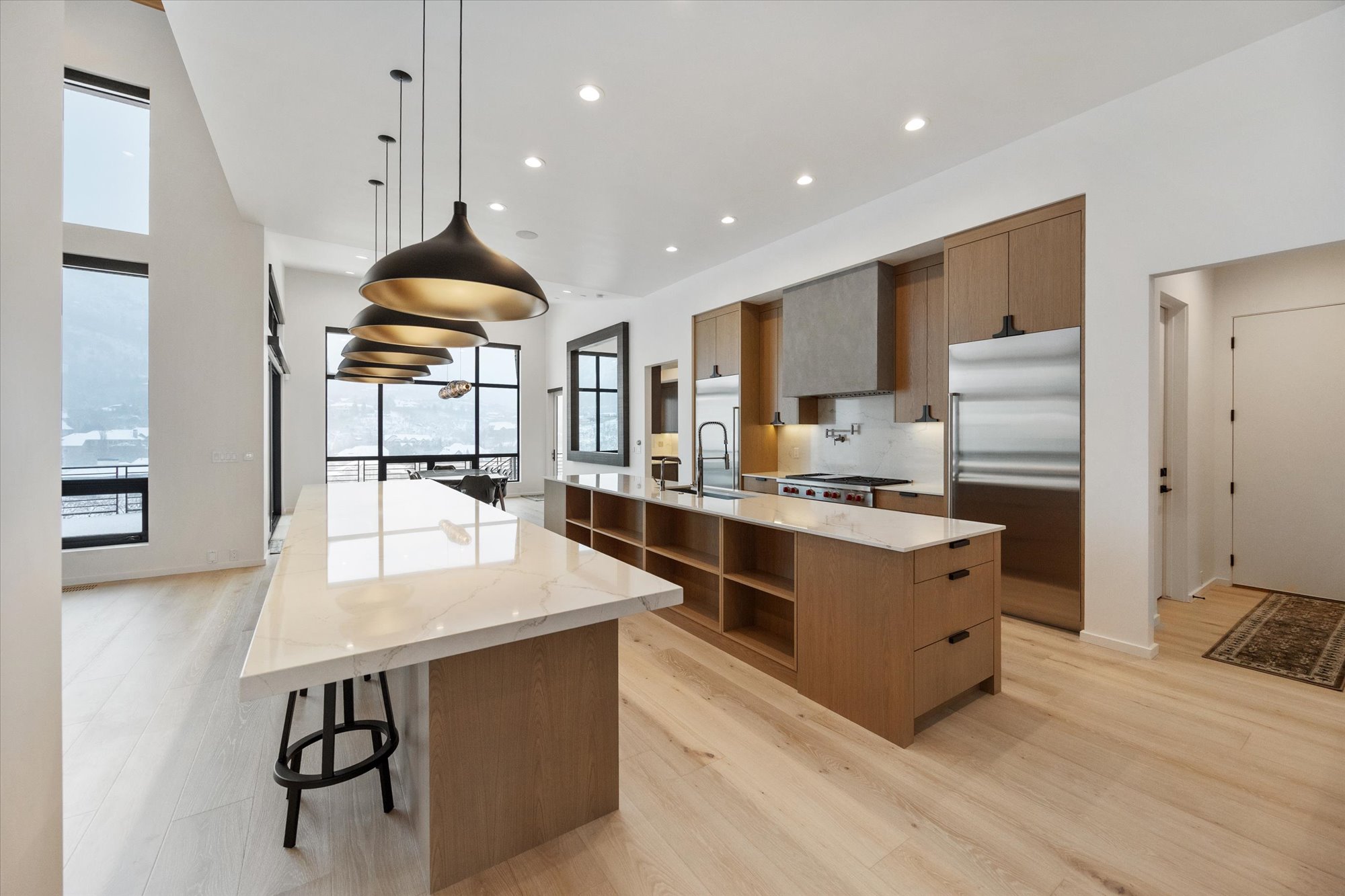 Kitchen featuring modern cabinets, stainless steel built in fridge, light stone countertops, and hanging light fixtures