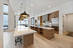 Kitchen featuring modern cabinets, stainless steel built in fridge, light stone countertops, and hanging light fixtures