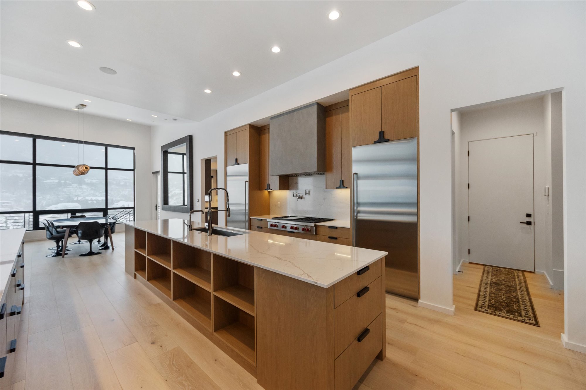 Kitchen featuring light stone counters, stainless steel appliances, a large island with sink, light wood-style floors, and wood finish cabinetry