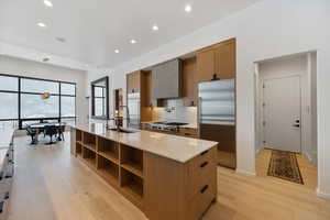 Kitchen featuring light stone counters, stainless steel appliances, a large island with sink, light wood-style floors, and wood finish cabinetry