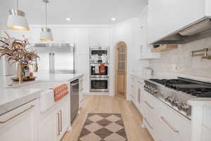 Kitchen with white cabinetry, built in appliances, light wood-style floors, and decorative light fixtures