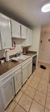 Kitchen with white cabinetry, light tile patterned flooring, and dishwashing machine