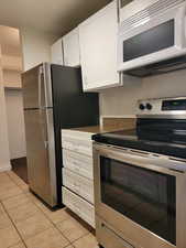 Kitchen featuring stainless steel appliances, white cabinets, light tile patterned flooring, and dark countertops