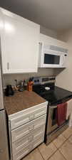 Kitchen featuring electric stove, white microwave, light tile patterned floors, white cabinets, and tile countertops