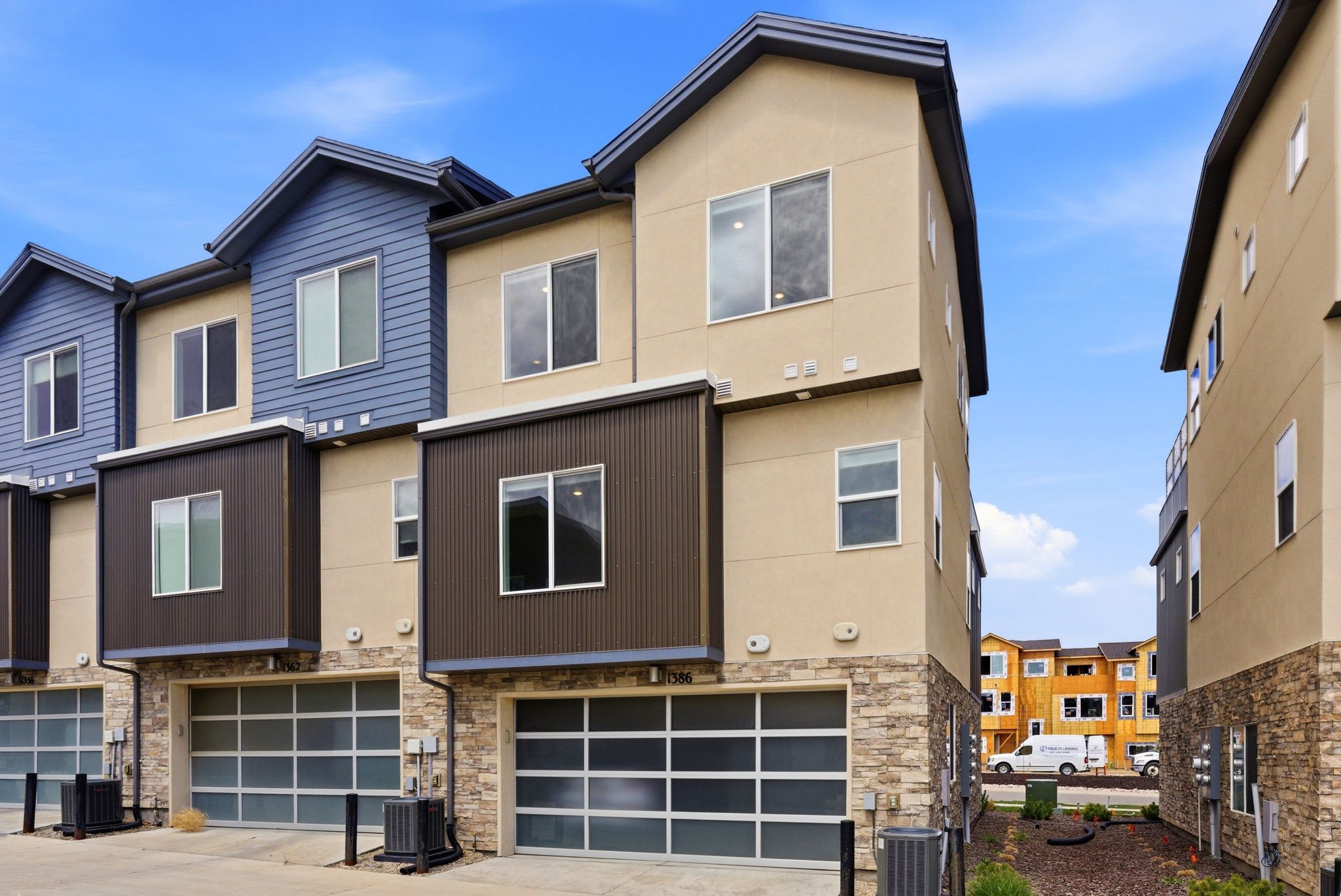 Modern home featuring stone siding, a garage, driveway, and stucco siding