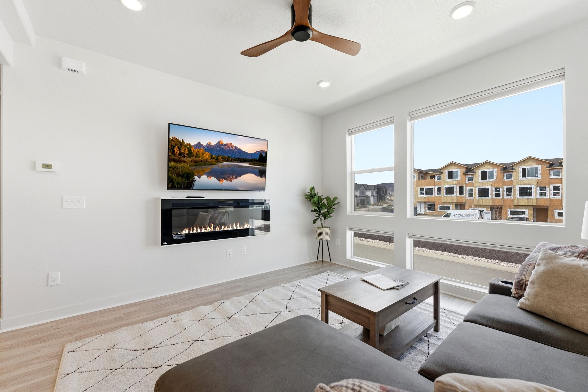 Living room with light wood-type flooring, a ceiling fan, a glass covered fireplace, and recessed lighting