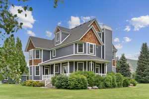 Back of house with covered porch, a lawn, and a shingled roof