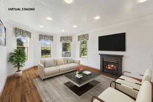 Living room featuring wood finished floors, a fireplace with flush hearth, ornamental molding, healthy amount of natural light, and a textured ceiling