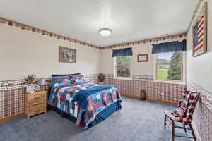 Bedroom featuring wallpapered walls, carpet, and a textured ceiling