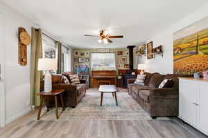 Living room with a wood stove, ceiling fan, and light wood-style floors