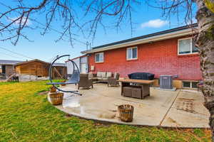 Rear view of house with outdoor lounge area, brick siding, a patio, a lawn, and an outbuilding