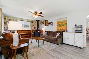 Living room with a wood stove, light wood-type flooring, and a ceiling fan