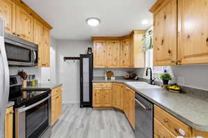 Kitchen featuring stainless steel appliances, dark countertops, light wood finish cabinetry, and recessed lighting