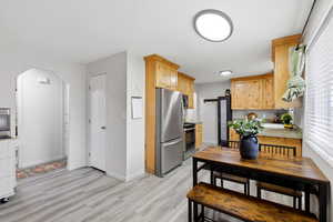 Kitchen with stainless steel appliances, light wood finish cabinets, light countertops, light wood-style flooring, and arched walkways