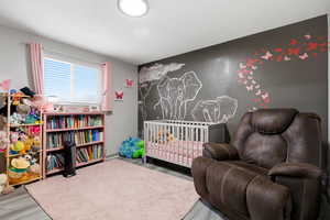 Bedroom with an accent wall, a crib, and light wood-style floors