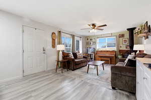 Living area featuring ceiling fan, light wood-style flooring, and a wood stove