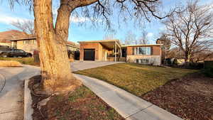 View of front facade featuring brick siding, driveway, a garage, and a chimney