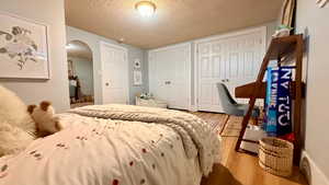 Bedroom with two closets, arched walkways, a textured ceiling, and wood finished floors
