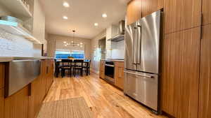Kitchen with modern cabinets, two tone cabinets, stainless steel appliances, light wood-style flooring, and suspended lighting