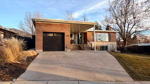 View of front facade featuring brick siding, a garage, driveway, and a chimney