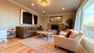 Living room featuring light wood-style floors, crown molding, a fireplace, and recessed lighting
