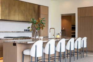 Kitchen with modern cabinets, a center island with sink, light stone counters, paneled built in fridge, and wood finish cabinetry