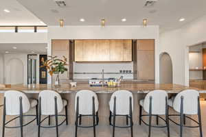 Kitchen with arched walkways, recessed lighting, modern cabinets, light wood finish cabinetry, and light stone counters