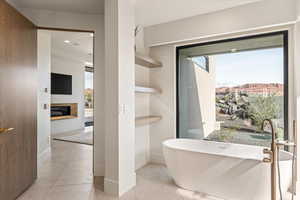 Bathroom featuring a freestanding bath, light tile patterned floors, recessed lighting, and a glass covered fireplace