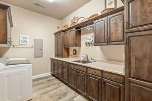 Laundry room featuring cabinet space, electric panel, light wood-style flooring, and washing machine and dryer