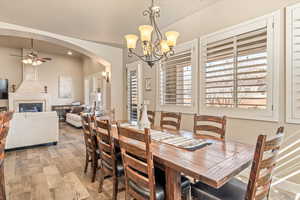 Dining space with hanging lights, ceiling fan, wood finished floors, a tiled fireplace, and arched walkways