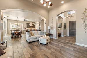 Living area with a ceiling fan, a chandelier, dark wood finished floors, and arched walkways