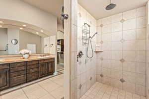 Full bathroom featuring double vanity, tiled shower, light tile patterned floors, and recessed lighting