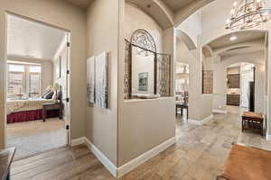 Hall featuring light wood-style flooring, suspended lighting, and arched walkways