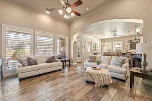 Living room with a ceiling fan, arched walkways, a chandelier, and wood-type flooring