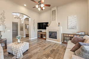 Living room with arched walkways, a high ceiling, light wood finished floors, a ceiling fan, and a tile fireplace