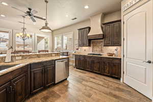 Kitchen featuring dark wood finish cabinets, dishwasher, dark wood-style flooring, light stone counters, and ceiling fan