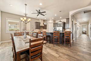 Dining room with ceiling fan, light wood-style floors, a chandelier, and arched walkways