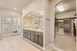 Full bath with a spacious closet, double vanity, recessed lighting, inlaid floor details, and light tile patterned floors