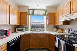 Kitchen with black appliances, light countertops, and wood finish cabinetry