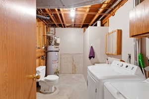 Half bathroom featuring laundry room, unfinished concrete floors, strapped water heater, and cabinet space