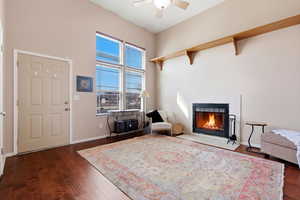 Living room featuring a fireplace, dark wood-style flooring, and ceiling fan
