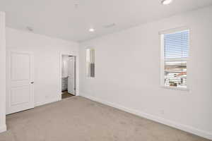 Unfurnished bedroom featuring light carpet, ensuite bathroom, and recessed lighting