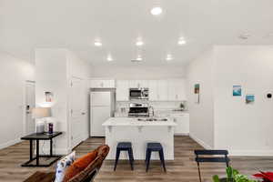 Kitchen with white cabinetry, a breakfast bar area, stainless steel appliances, dark wood-type flooring, and a kitchen island with sink