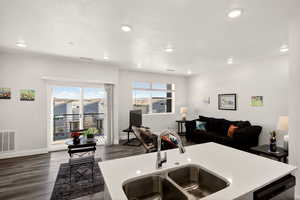 Kitchen featuring dark wood finished floors, open floor plan, light countertops, a kitchen island with sink, and stainless steel dishwasher