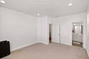 Unfurnished bedroom featuring light colored carpet, ensuite bath, and recessed lighting